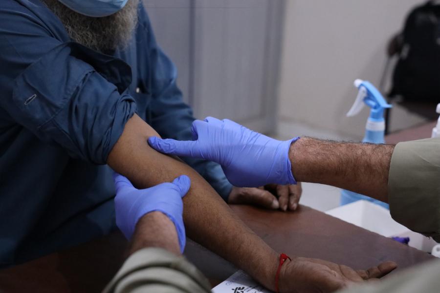 Pair of hands of MSF staff taking blood sample from a patient's arm for a PCR test.